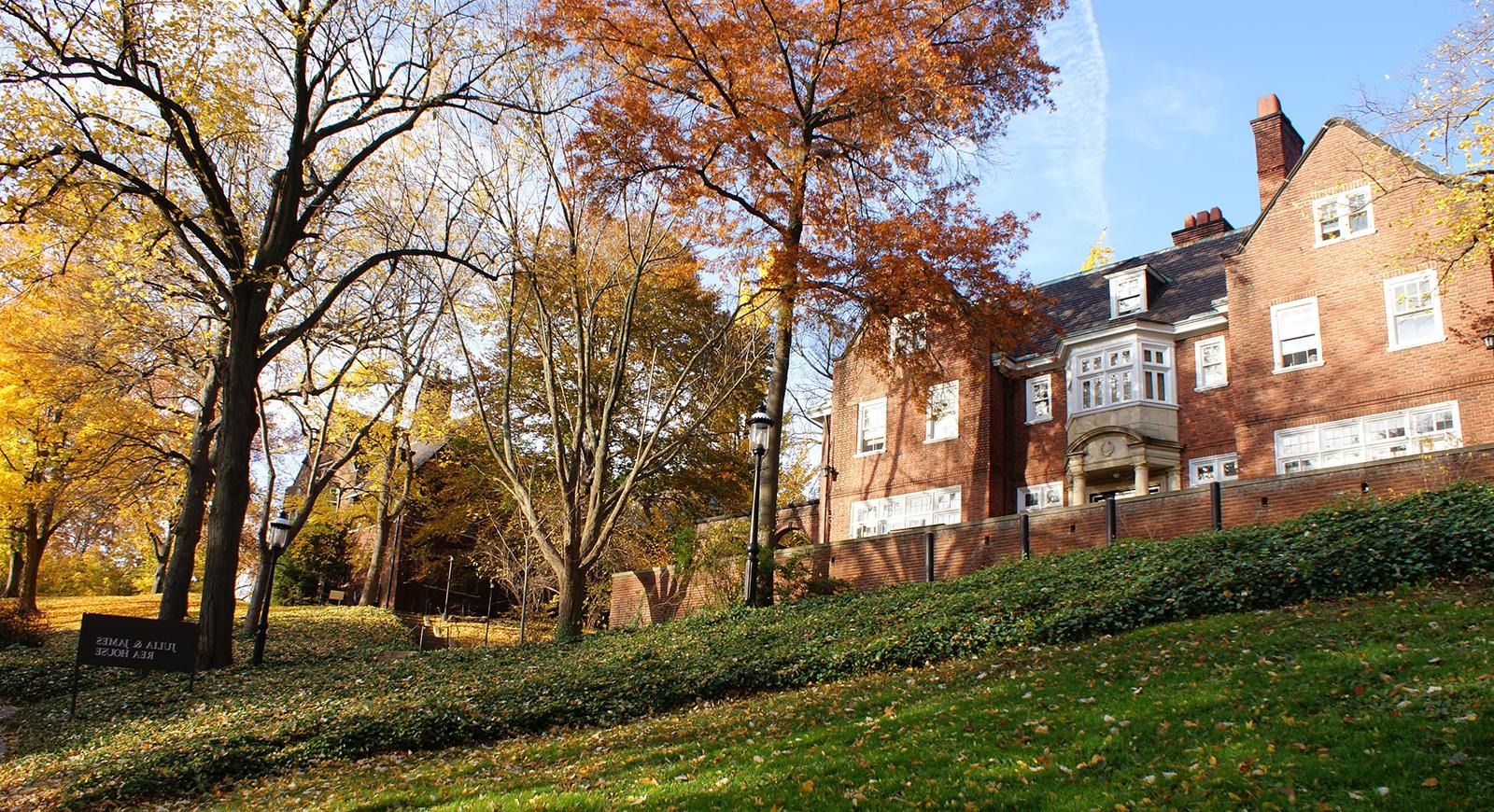 Photo of Julia and James Rea House, atop a grassy hill covered in multicolored fall leaves on Chatham University's Shadyside Campus. 
